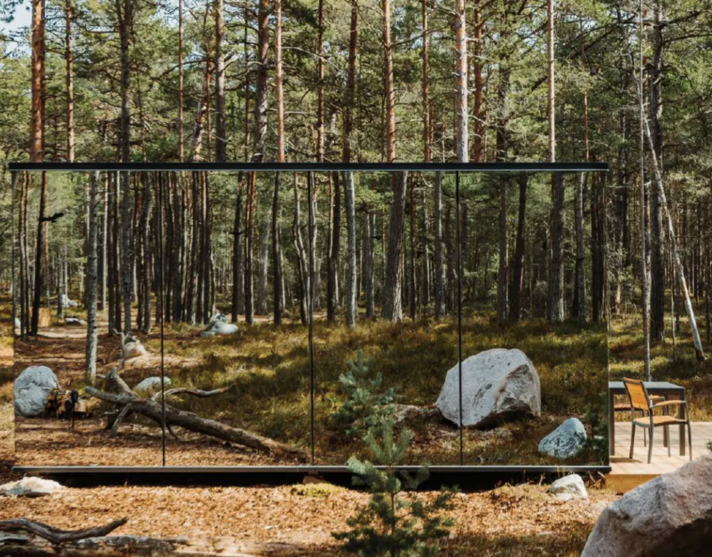 A cabin with mirror-reflecting walls nestled in a pine forest.